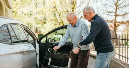 Eine Person hilft einem älteren Mann beim Einsteigen ins Auto